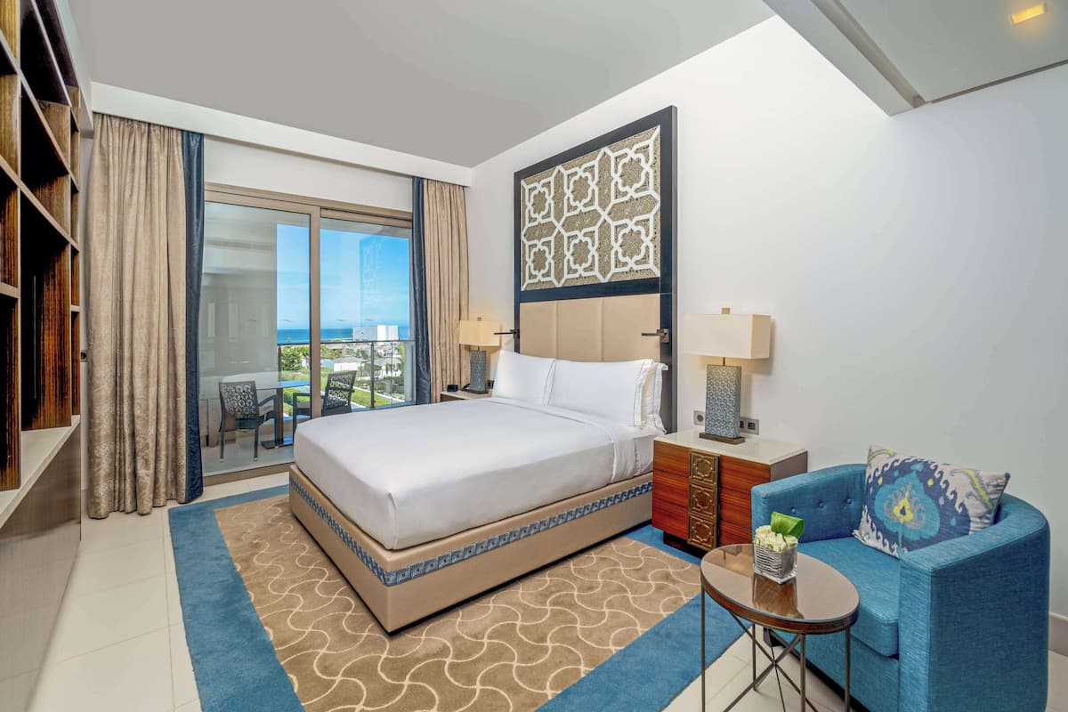 Une chambre d’hôtel avec un grand lit, un canapé bleu, une petite table et une vue sur la ville par une grande fenêtre.