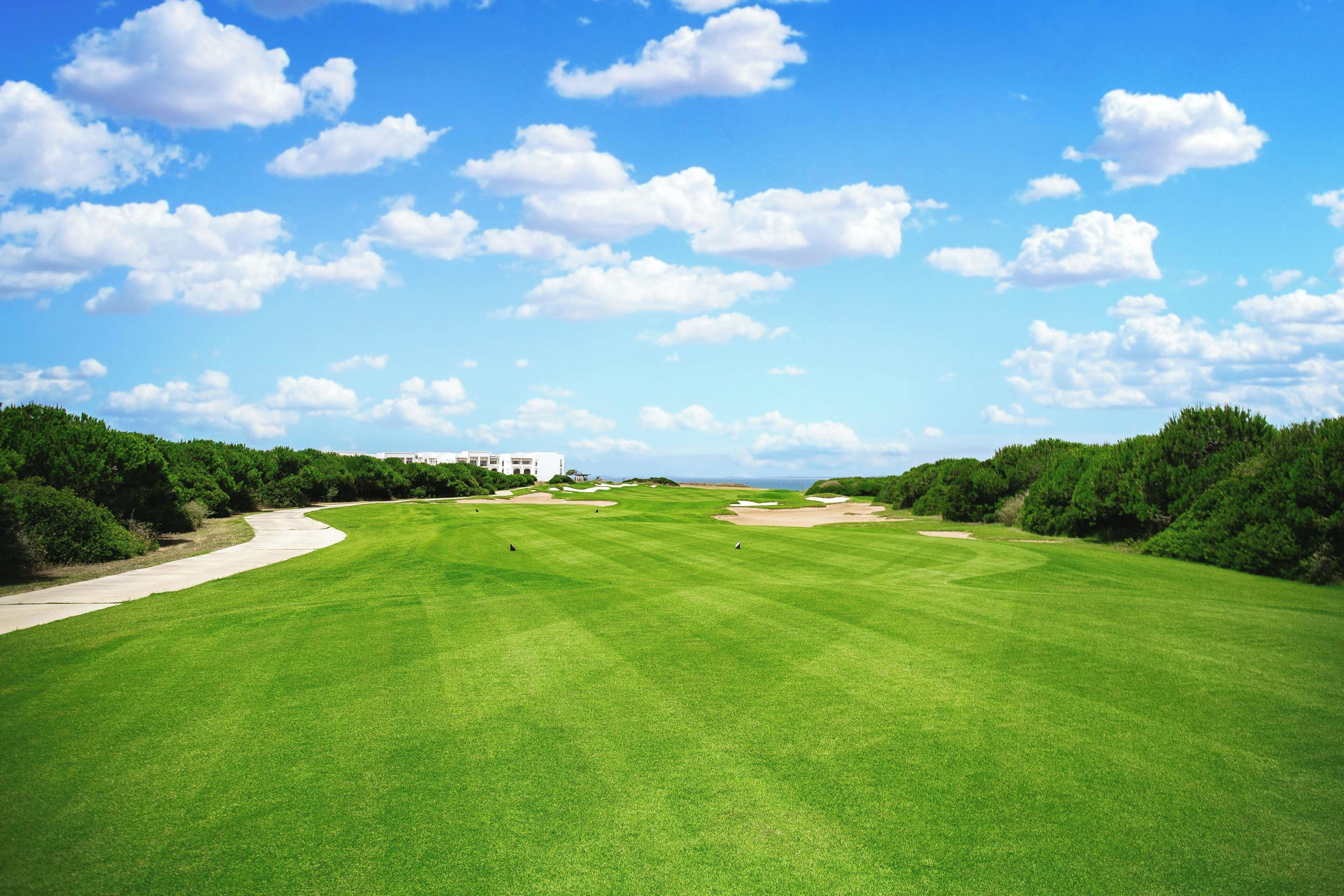 Un campo de golf bajo un cielo despejado y nubes dispersas.
