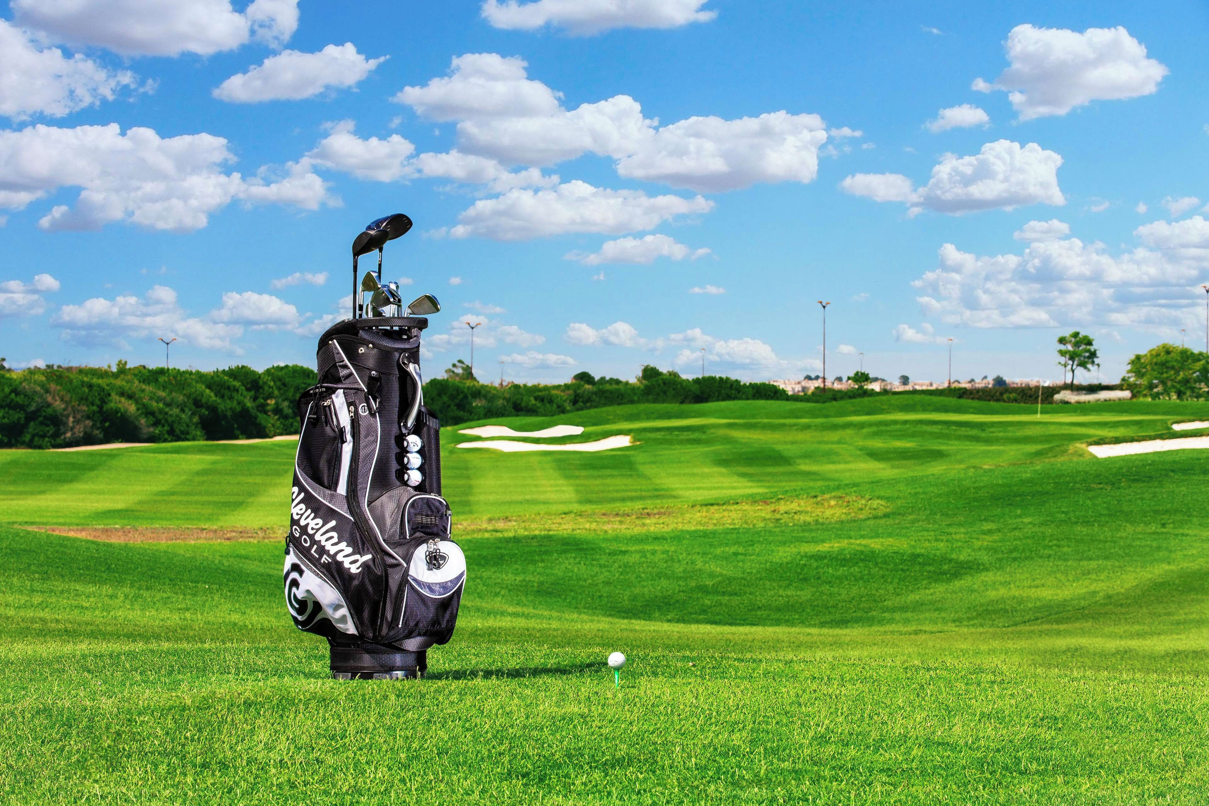 Un bolso de golf sobre un campo verde, con cielo despejado y nubes.