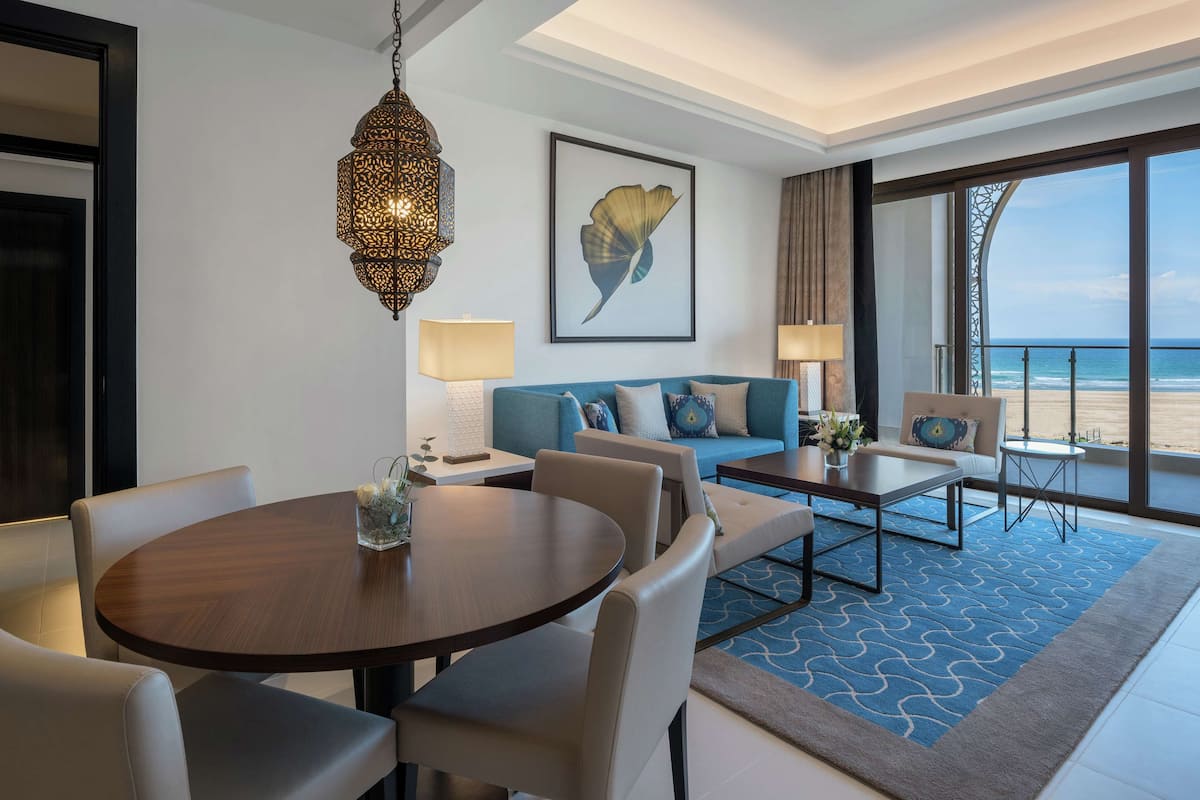 Une chambre d’hôtel comprenant un coin repas, un ensemble de canapés, une grande fenêtre donnant sur la plage et un élément décoratif mural.