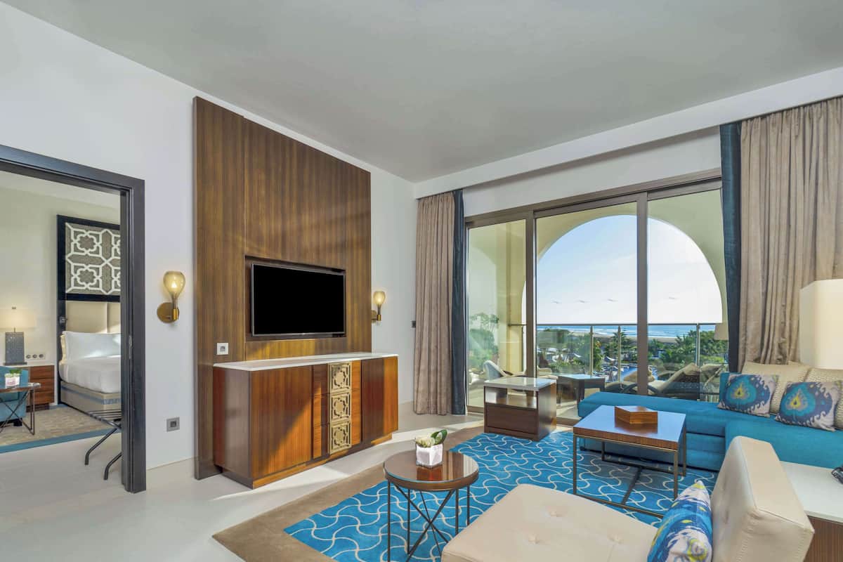 Une chambre d’hôtel dotée d’une grande télévision, d’un canapé, d’une table basse et offrant une vue sur l’océan.