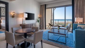 Ett modernt hotellrum med en matplats, en platt-TV och en balkong med utsikt över stranden.