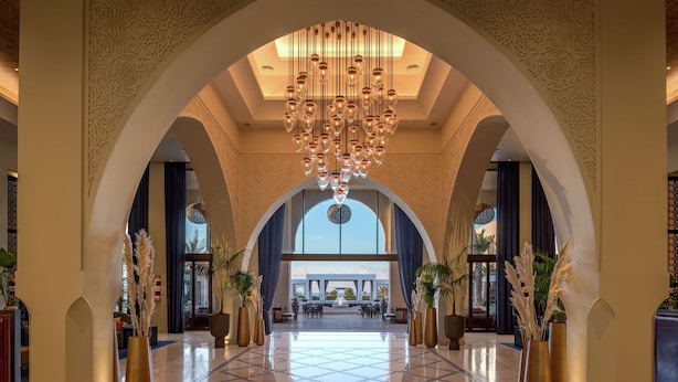 A spacious lobby with a high ceiling, a large chandelier, and a view through the arched doorway.