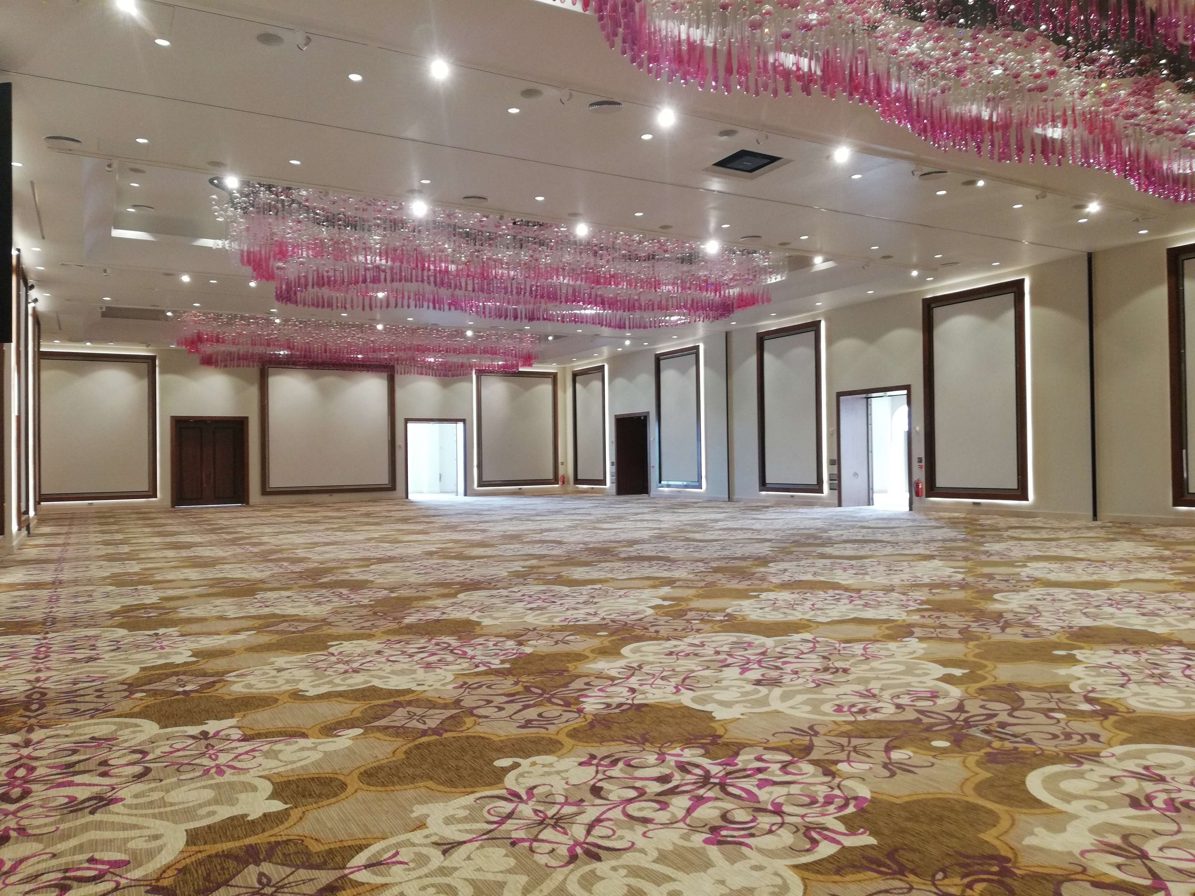 A spacious hotel room with a patterned carpet, large windows, and a ceiling adorned with hanging decorations.