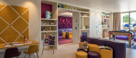 A modern children's playroom with a large table, chairs, and a sofa.