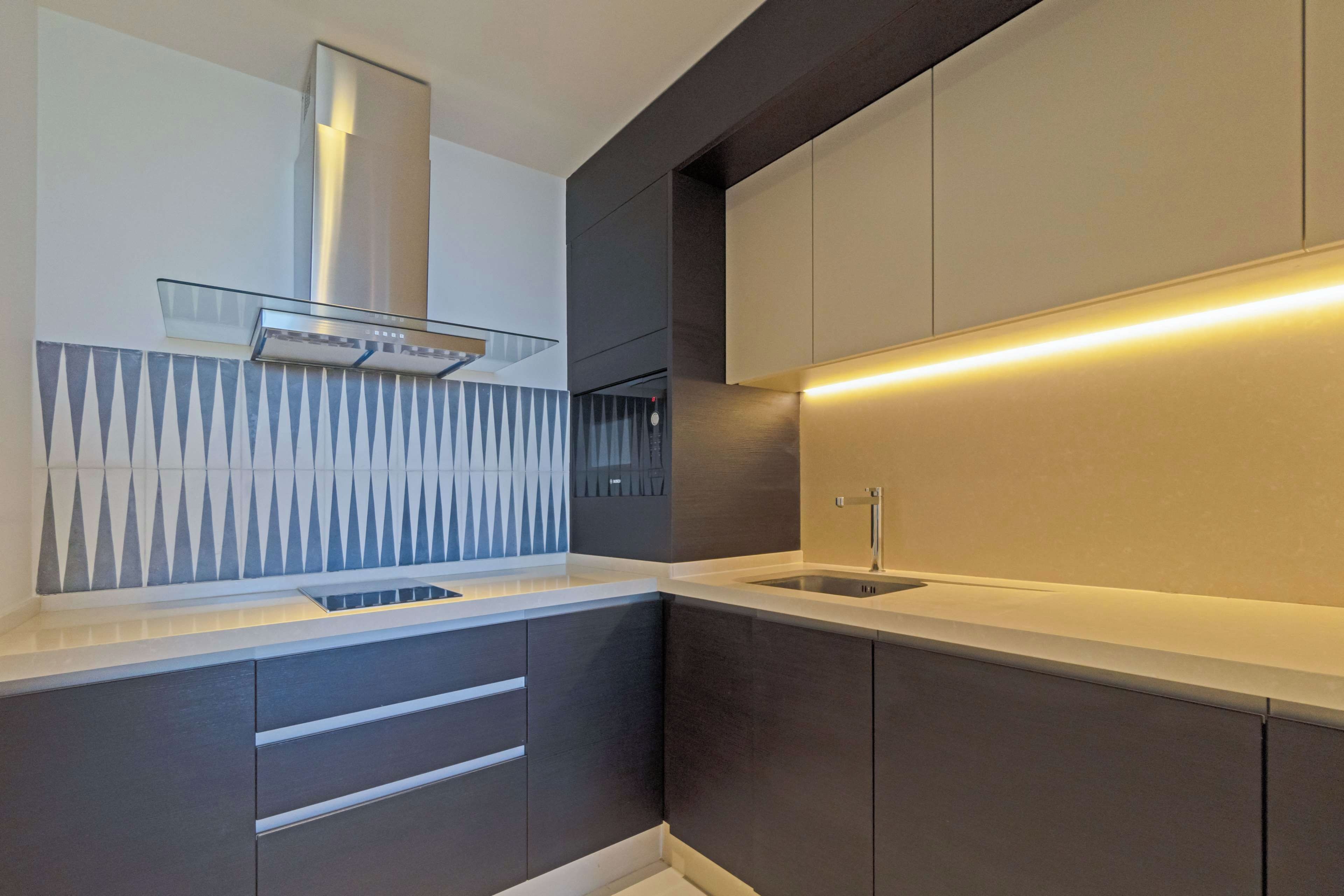 A modern kitchen with dark cabinetry, a stainless steel range hood, and a sleek countertop.