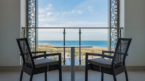 A balcony with two wicker chairs and a table, overlooking a beach and ocean.
