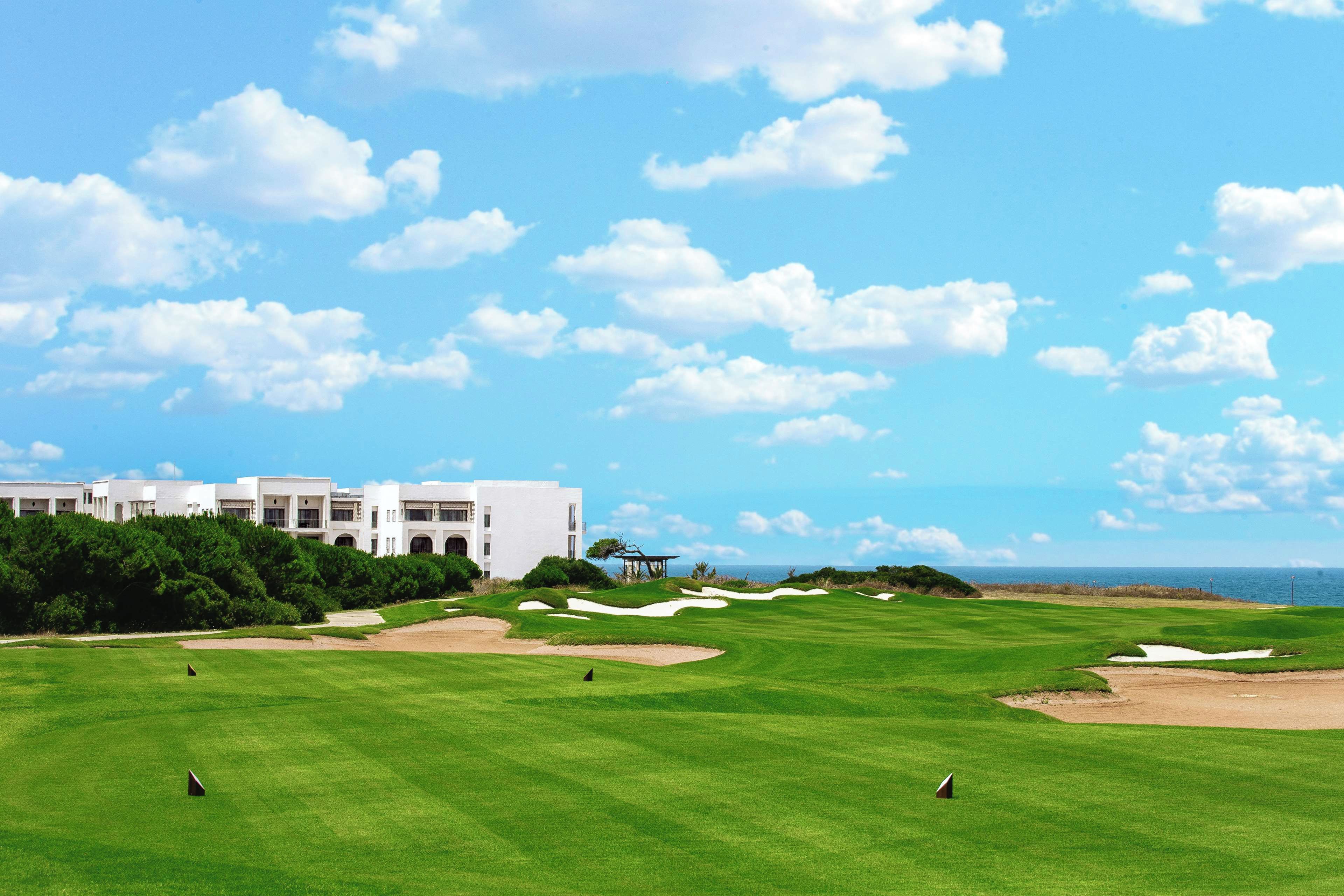 Campo de golfe com bunkers e um edifício ao fundo.