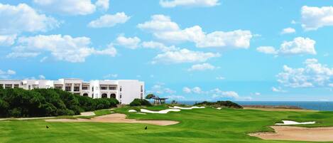 Campo de golfe com bunkers e um edifício ao fundo.