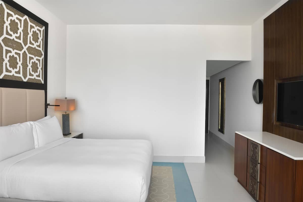 Une chambre d’hôtel avec un grand lit, une table de chevet avec une lampe, un téléviseur fixé au mur et une armoire en bois.
