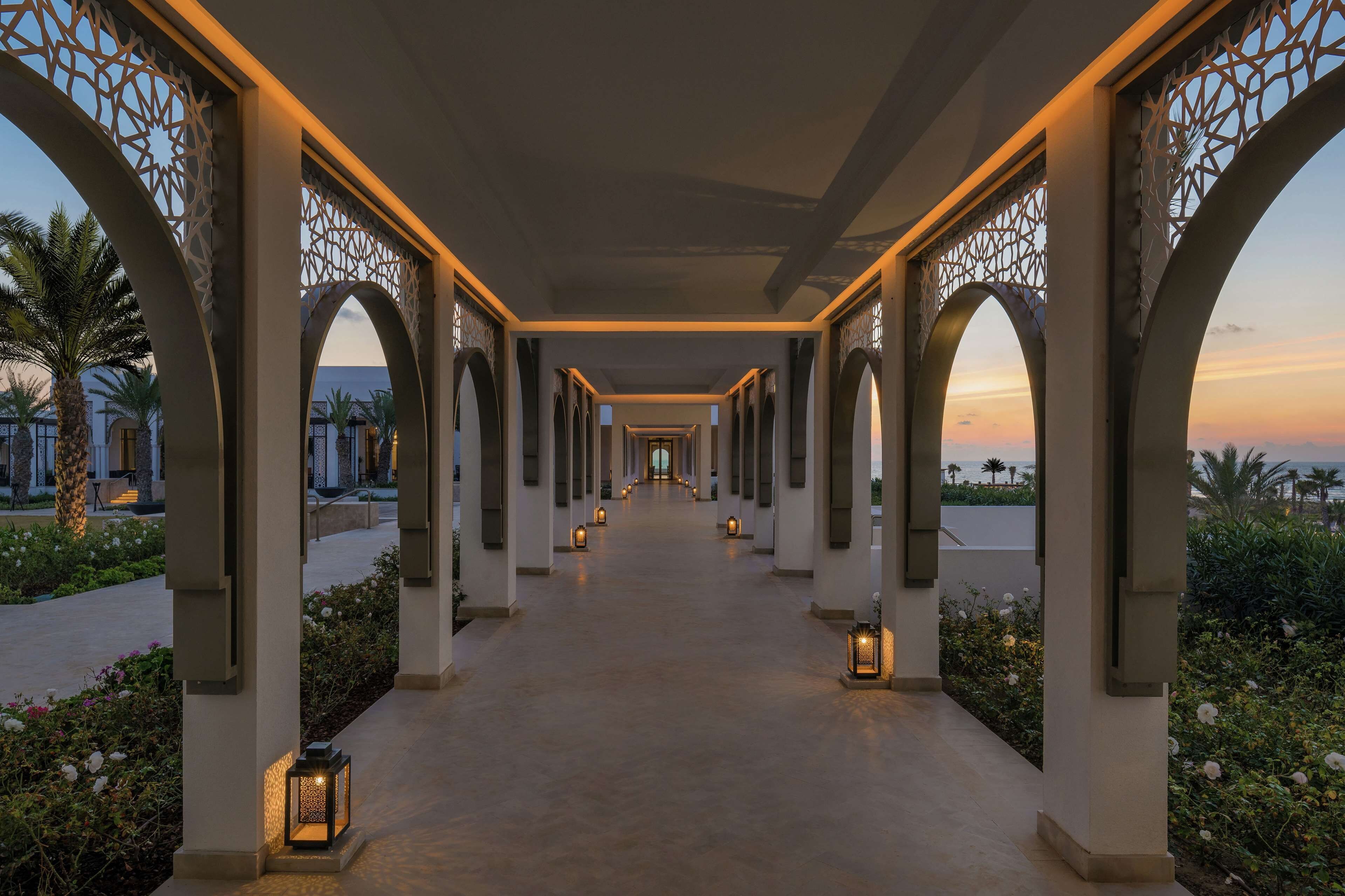 A corridor with arches and lanterns, leading to a distant view.