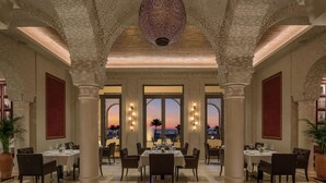 A spacious dining area with high ceilings, large windows, and a view of the sunset.