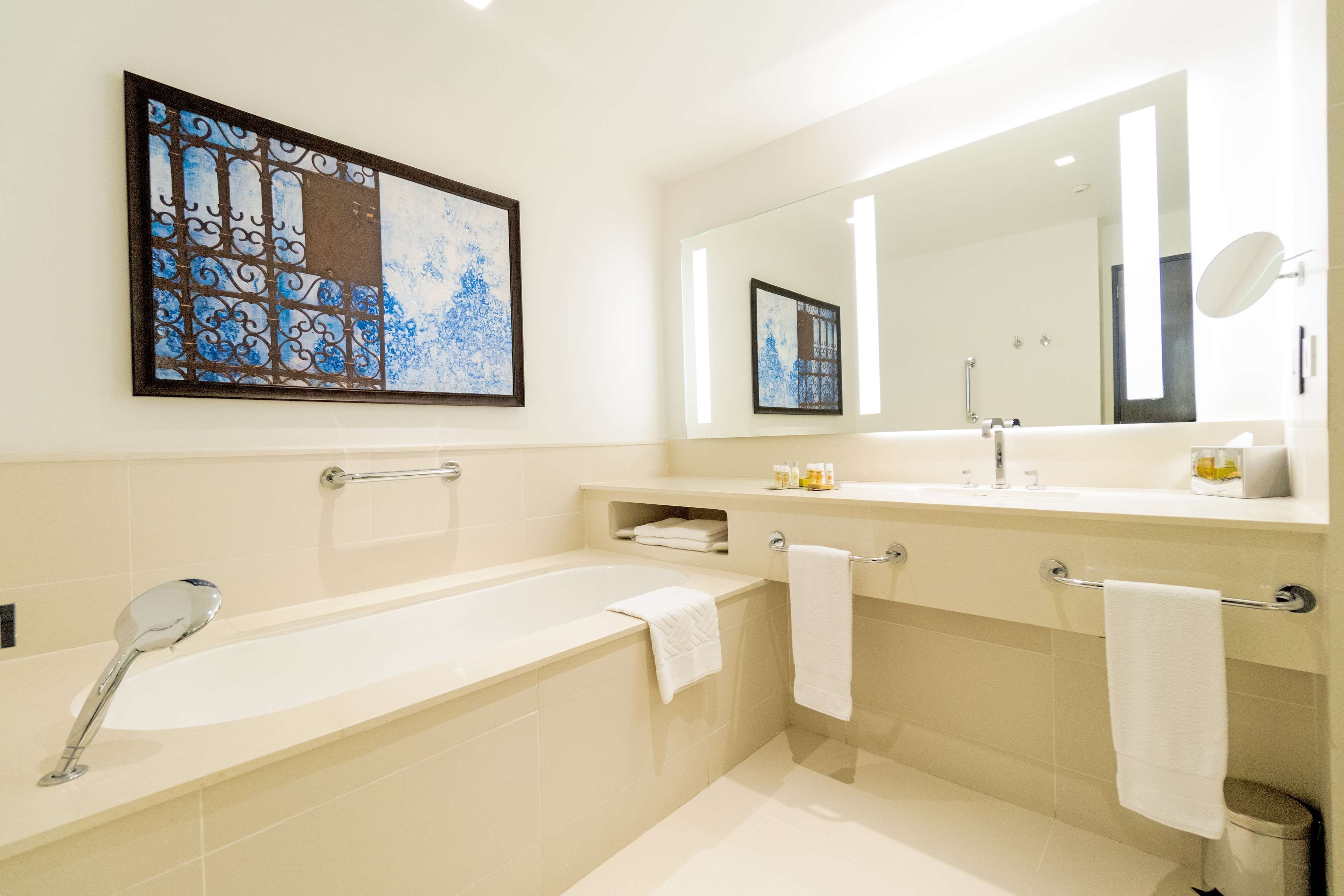 A modern bathroom with a bathtub, a large mirror, and a framed artwork on the wall.