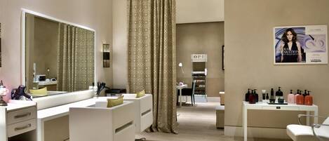 A modern bathroom with a large mirror, vanity with multiple sinks, and a hairdryer. There is a poster on the wall and a shelf with various toiletries.