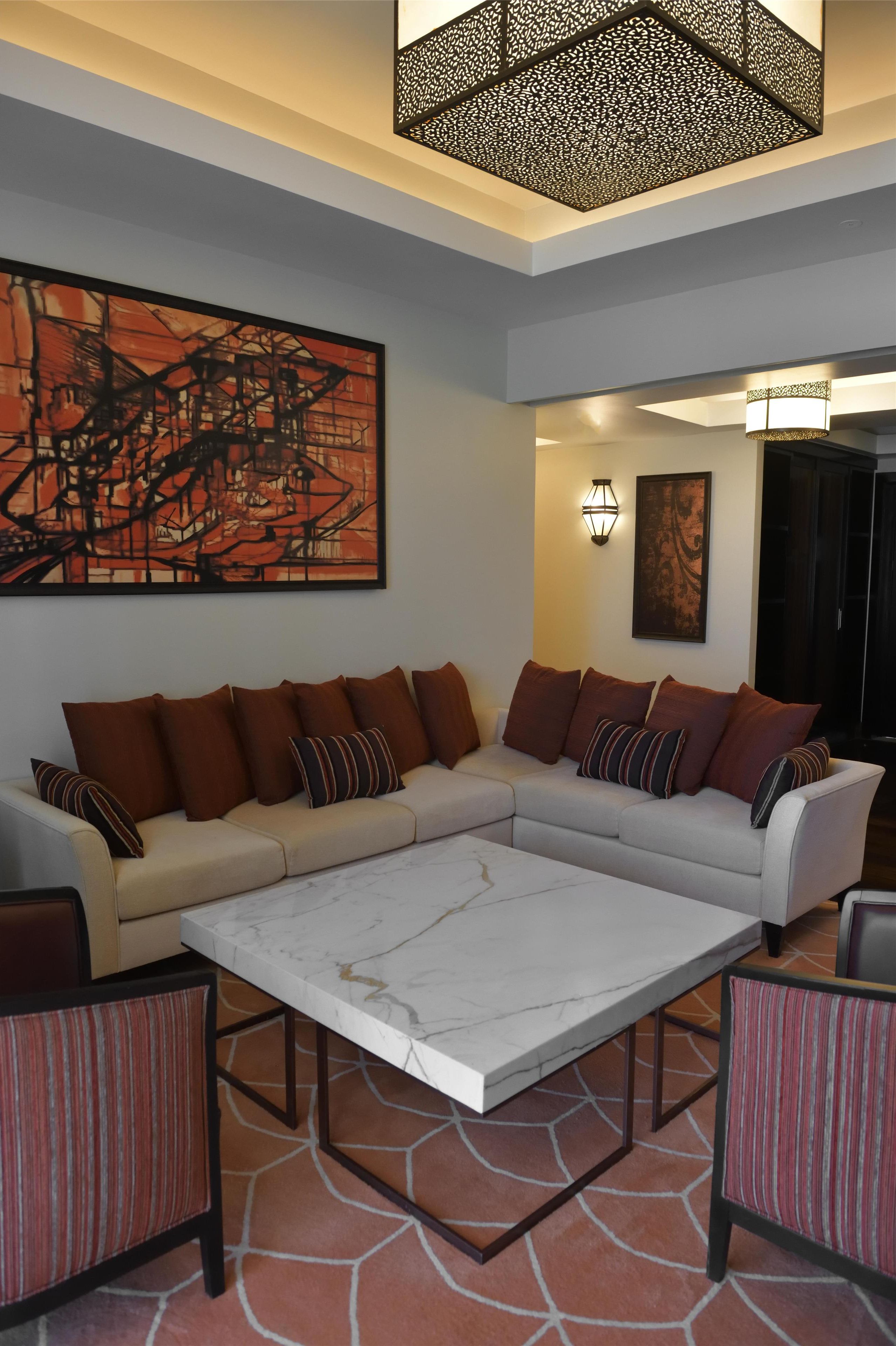A modern living room with a sectional sofa, a marble coffee table, striped armchairs, and abstract art on the walls.