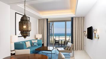A hotel room with a large window offering a view of the beach, a blue sofa, a wooden dining table, and a hanging lantern.