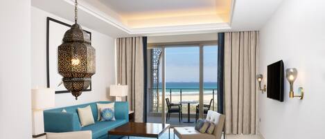 A hotel room with a large window offering a view of the beach, a blue sofa, a wooden dining table, and a hanging lantern.