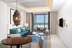 A hotel room with a large window offering a view of the beach, a blue sofa, a wooden dining table, and a hanging lantern. - Hilton Tangier Al Houara Resort & Spa (Hjar Ennhal)