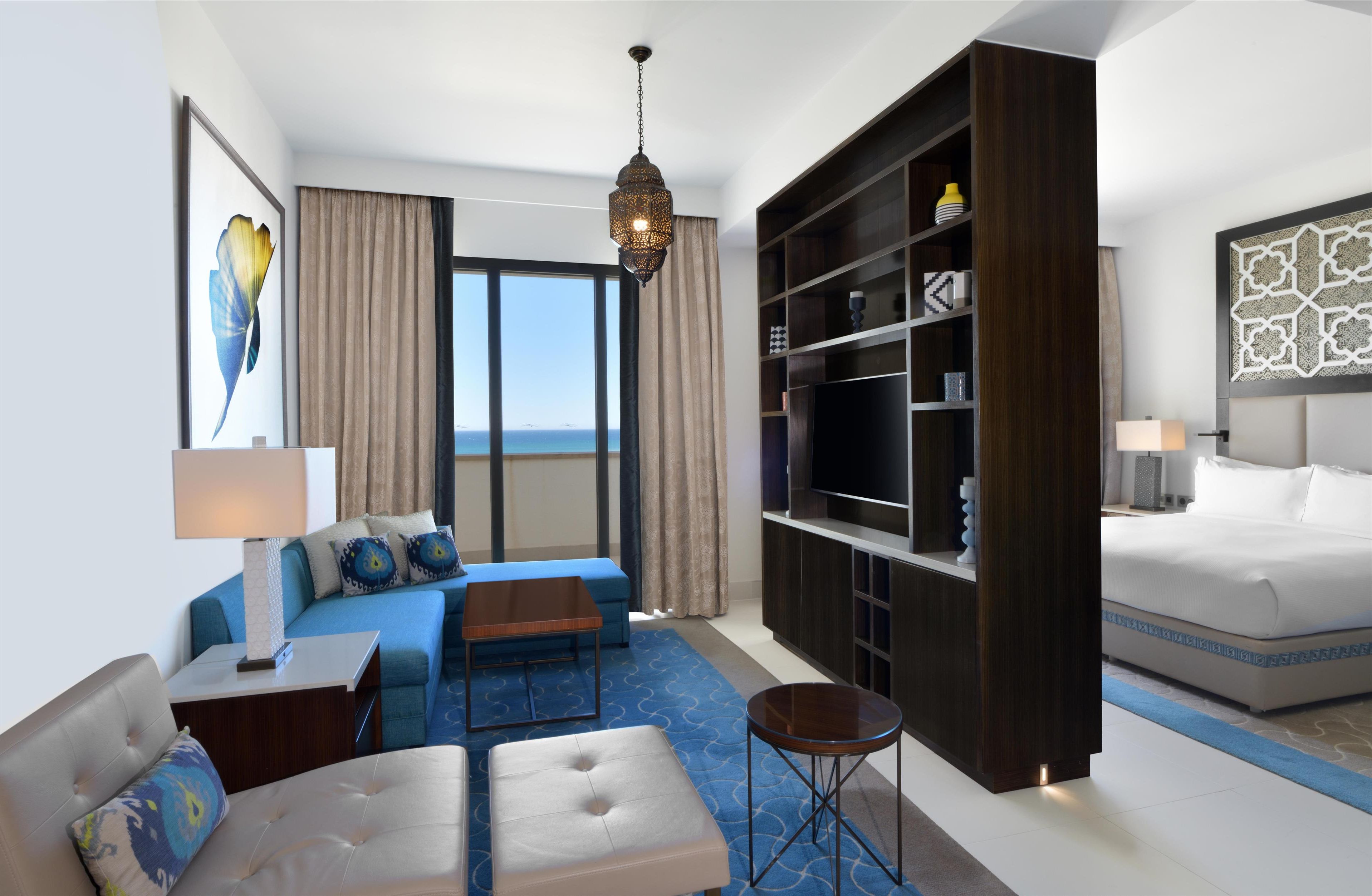 Una habitación de hotel moderna con una cama grande, un sofá, una mesita de centro, un televisor y una estantería.