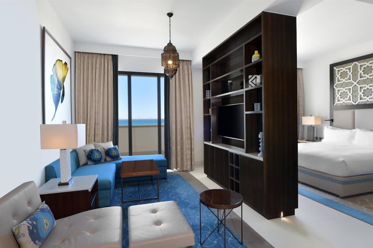 Une chambre d’hôtel moderne avec un grand lit, un canapé, une table basse, une télévision et une bibliothèque.
