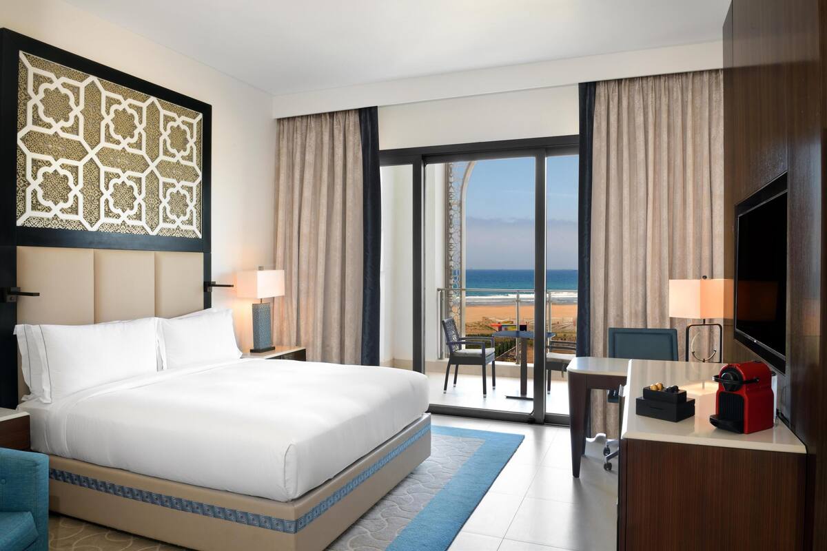 Une chambre d’hôtel avec un grand lit, un bureau, une télévision et une vue sur la plage.