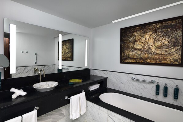 A modern bathroom with a black countertop, a white sink, a large mirror, and a bathtub.