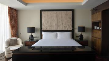 Een moderne hotelkamer met een groot bed, twee nachtkastjes met lampen, een houten garderobe en een kamerbreed gordijn met patroon.