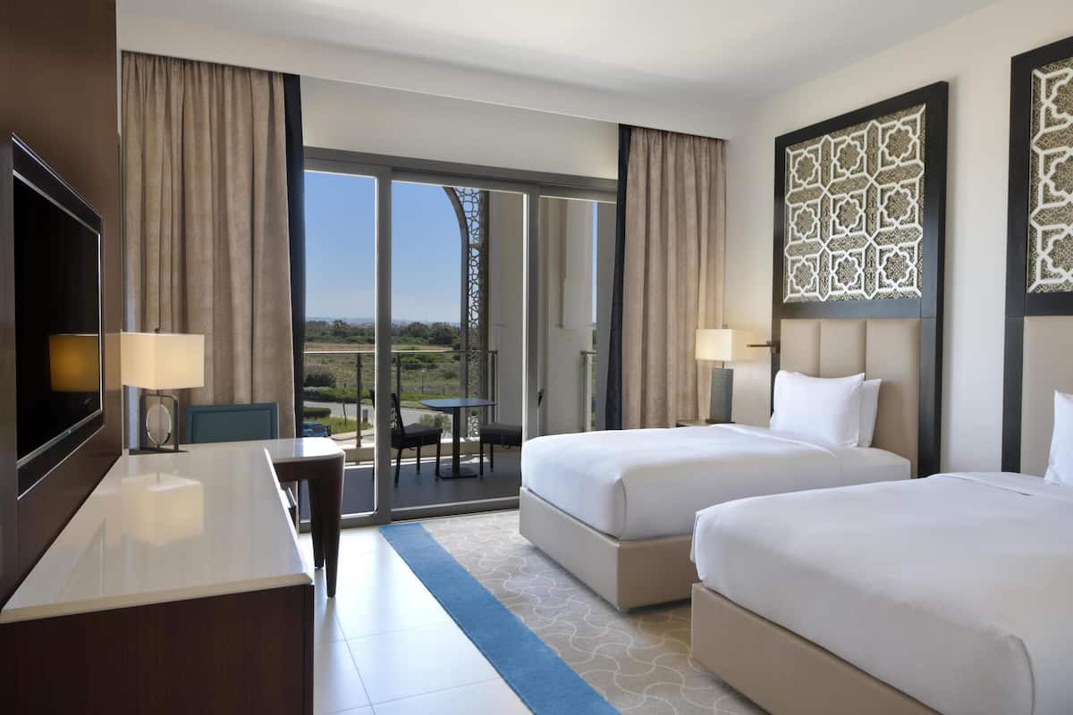 Une chambre d’hôtel avec deux lits, un bureau, une télévision et un balcon avec vue.