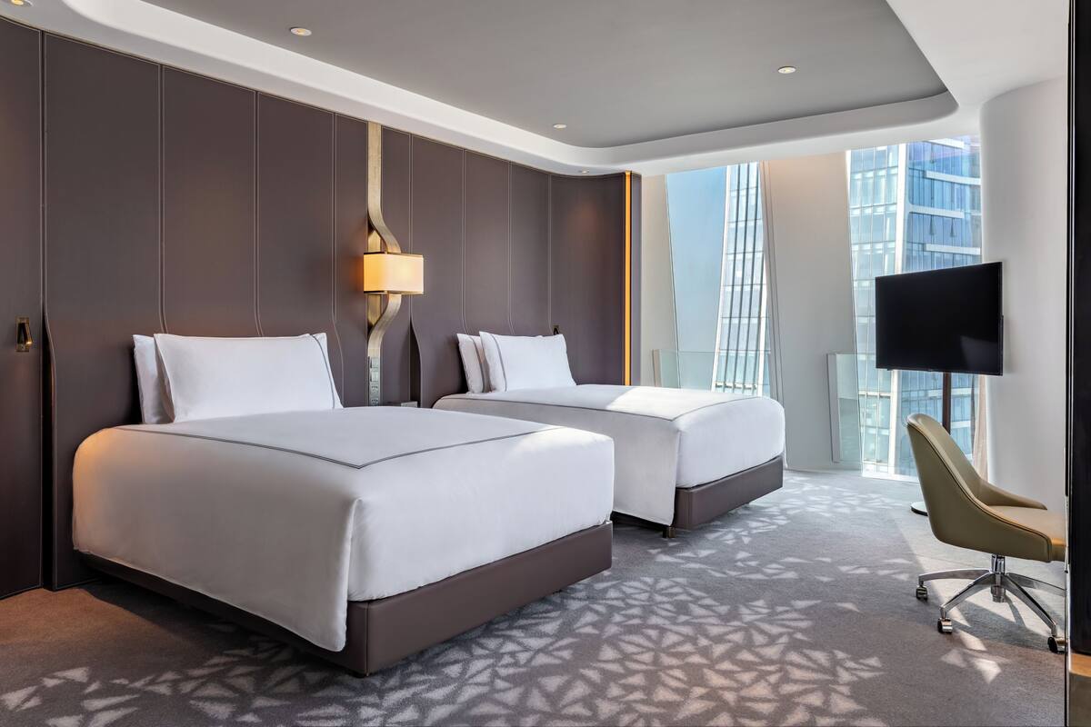 A hotel room with two beds, a TV, and a chair.