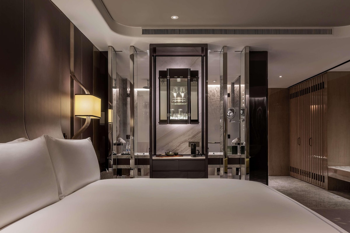 A modern hotel room with a large bed, a vanity with a mirror, and a walk-in closet.
