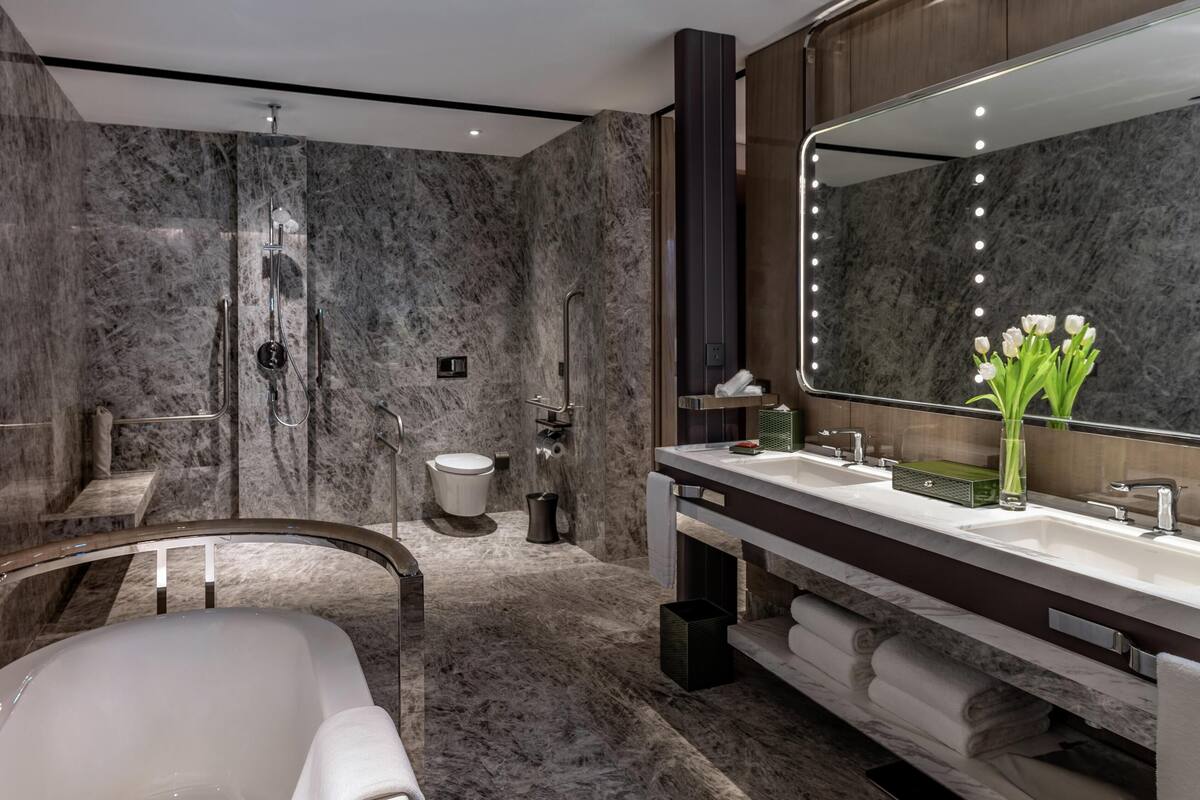 A modern bathroom with a marble shower, a bathtub, and a vanity with a large mirror.