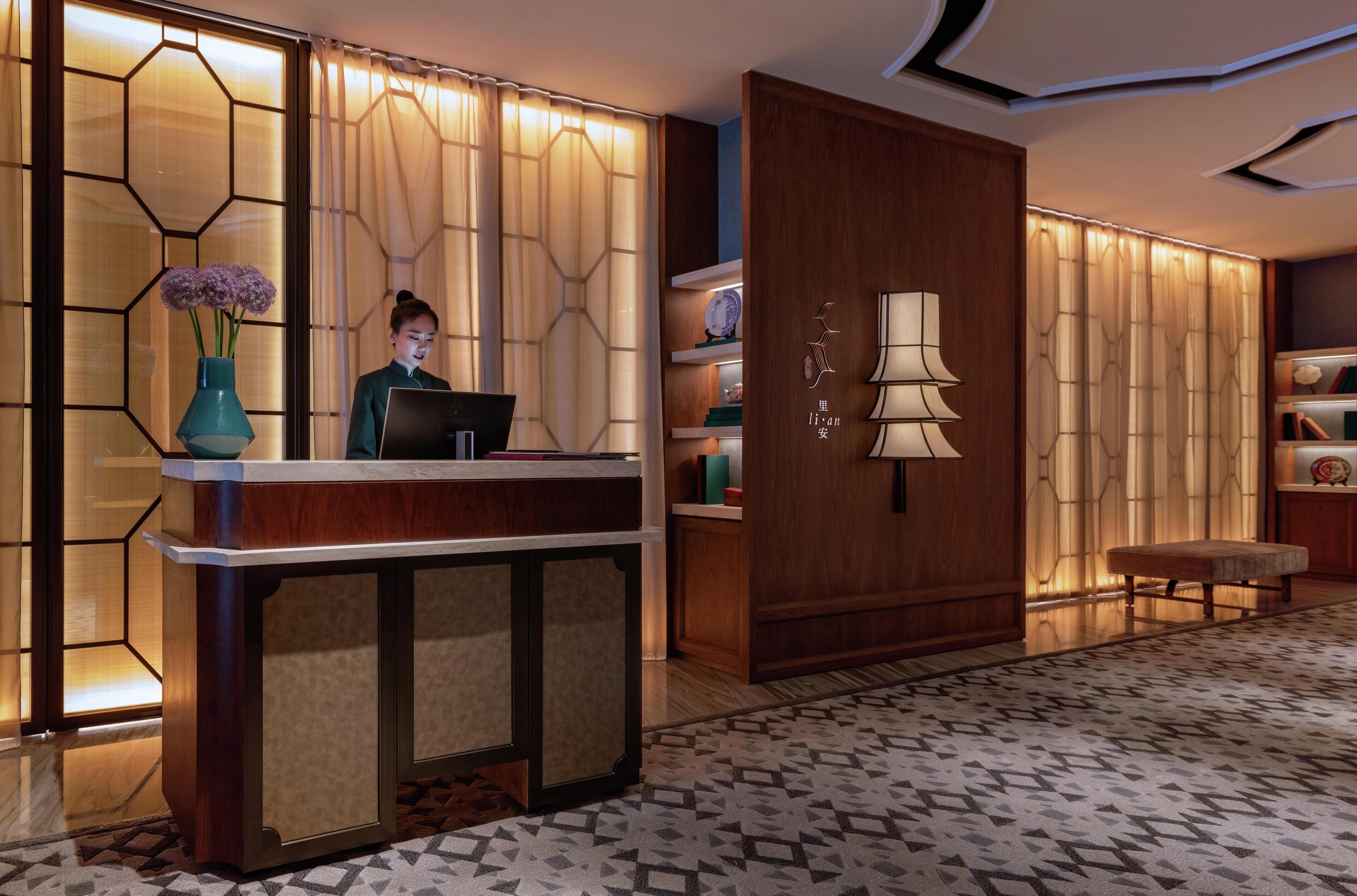 A reception area with a wooden reception desk, a vase with flowers, and a wall-mounted lamp.
