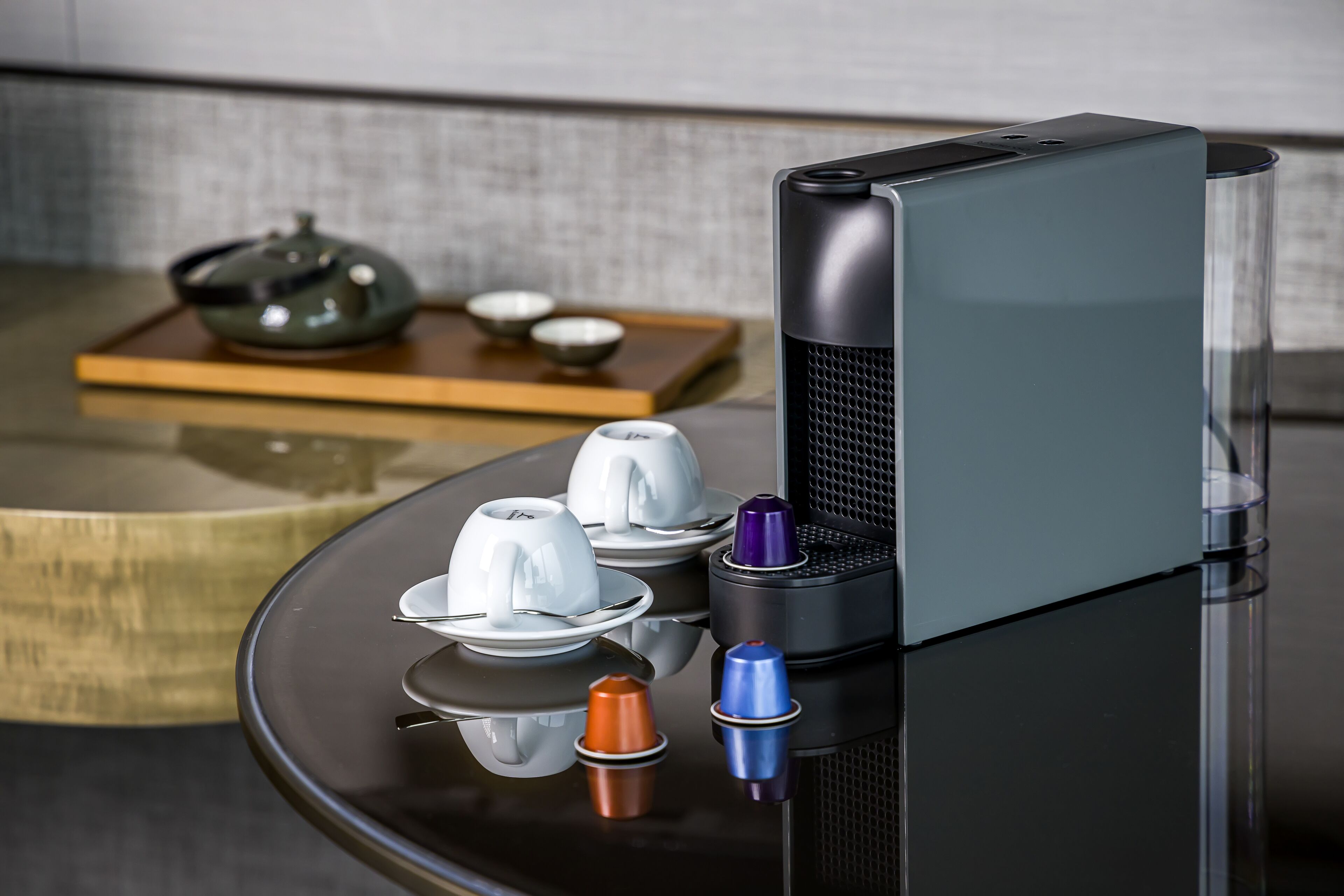 Une cuisine moderne avec un élégant plan de travail noir, une bouilloire en acier inoxydable, des tasses à thé blanches et une machine à café.