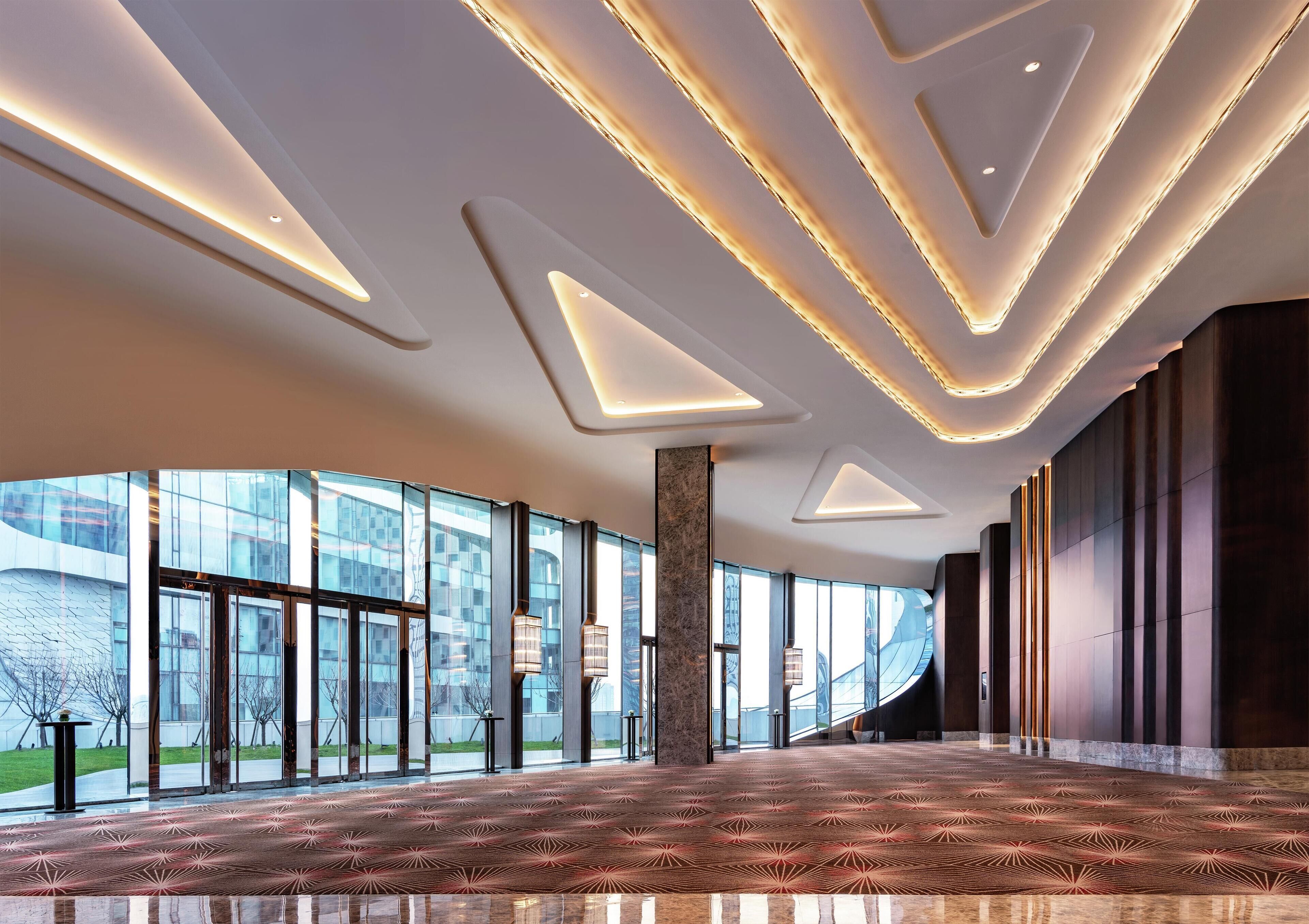 Un'ampia hall con tappeto decorato, grandi finestre e lampade moderne.