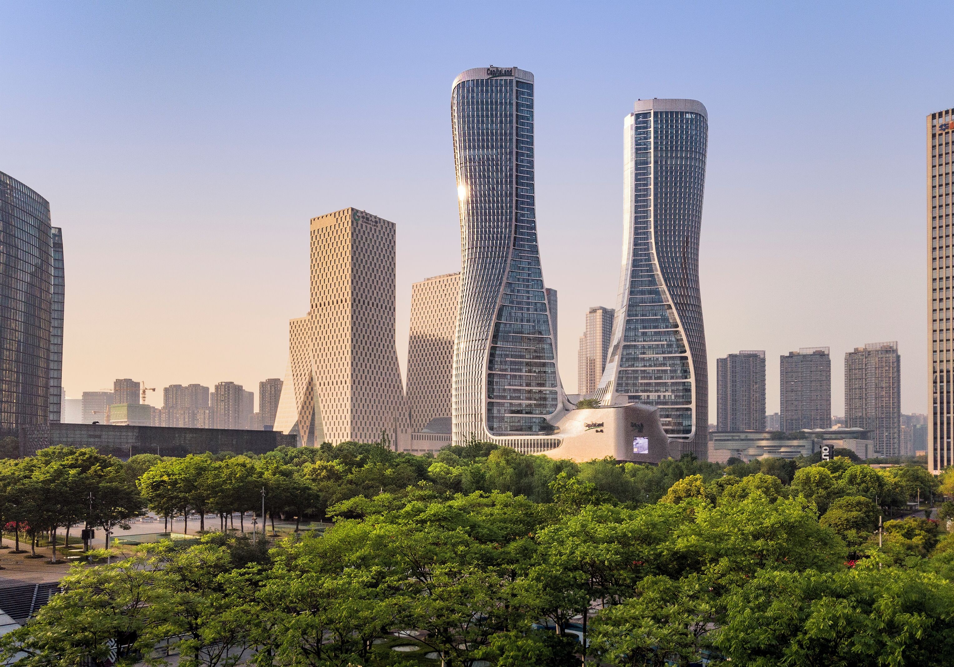 Un paysage urbain avec des gratte-ciel modernes, un parc arboré et un ciel dégagé.