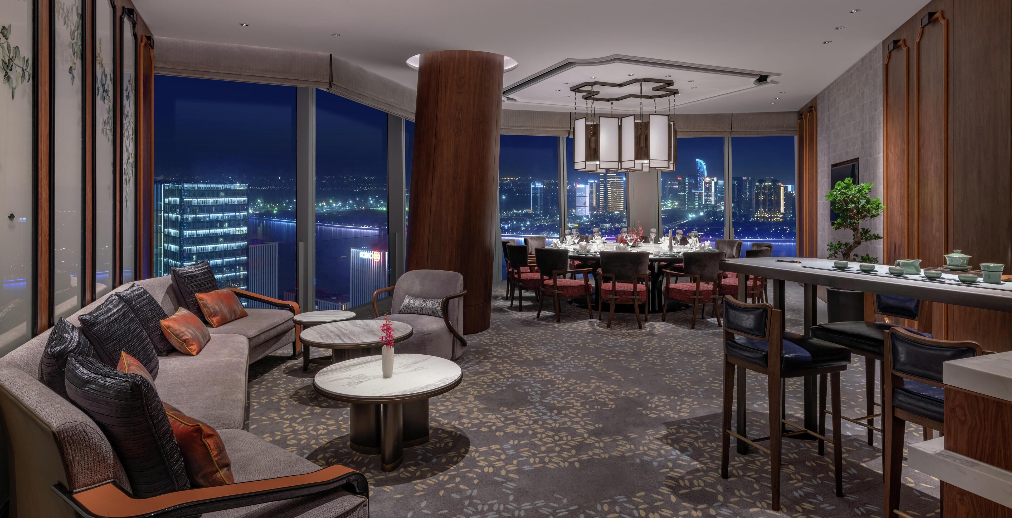 Un moderno vestíbulo de hotel con vista a la ciudad, un comedor y un área de descanso con sofá y mesa de centro.