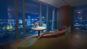 A modern interior with a curved sofa, a small round table with a vase, and a cityscape view through large windows. - Conrad Hangzhou (Hangzhou)