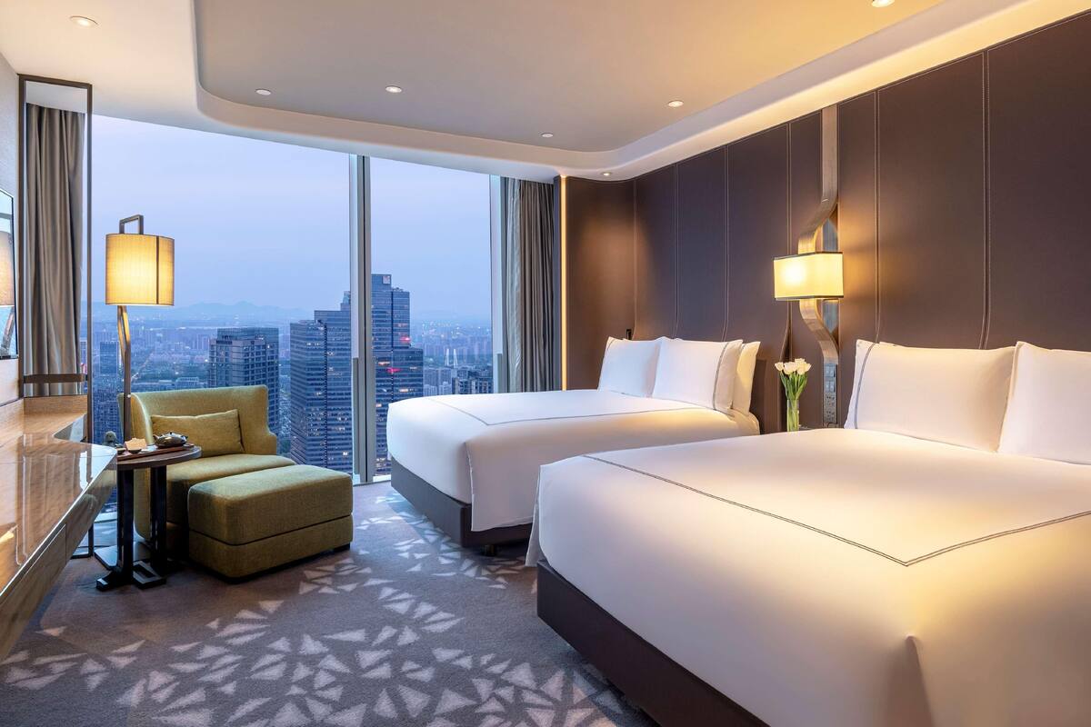 Ein Hotelzimmer mit zwei Betten, einer Sitzecke, einem Schreibtisch und Blick auf die Stadt.