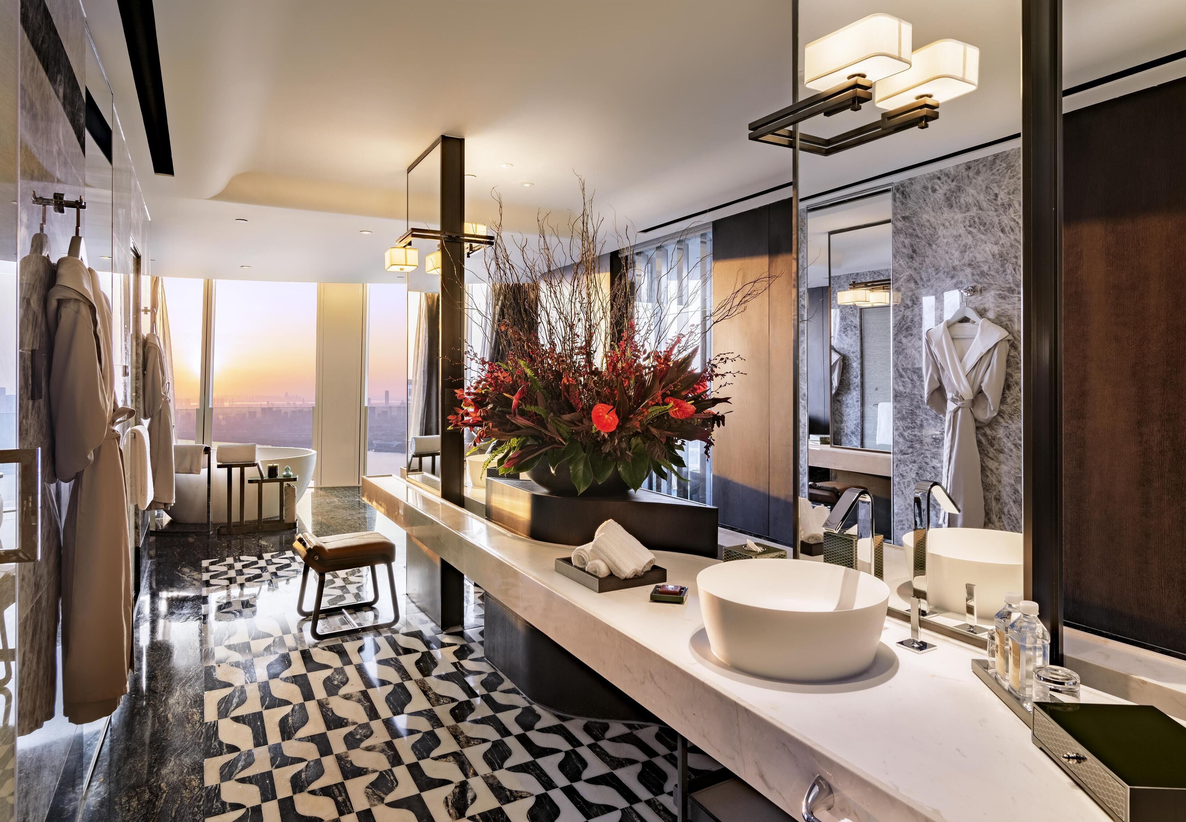 A modern bathroom with a large mirror, a white sink, and a decorative plant.