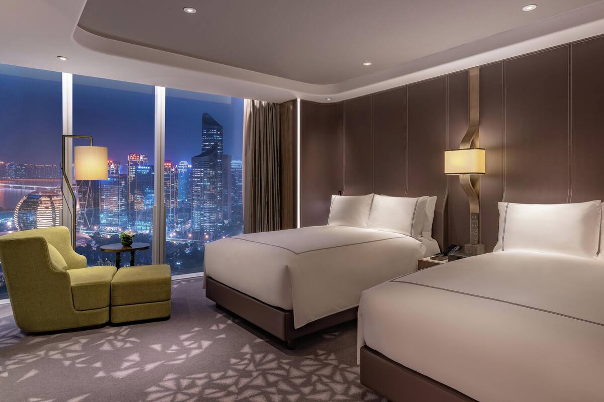 A hotel room with two beds, a sofa, and a view of the cityscape.