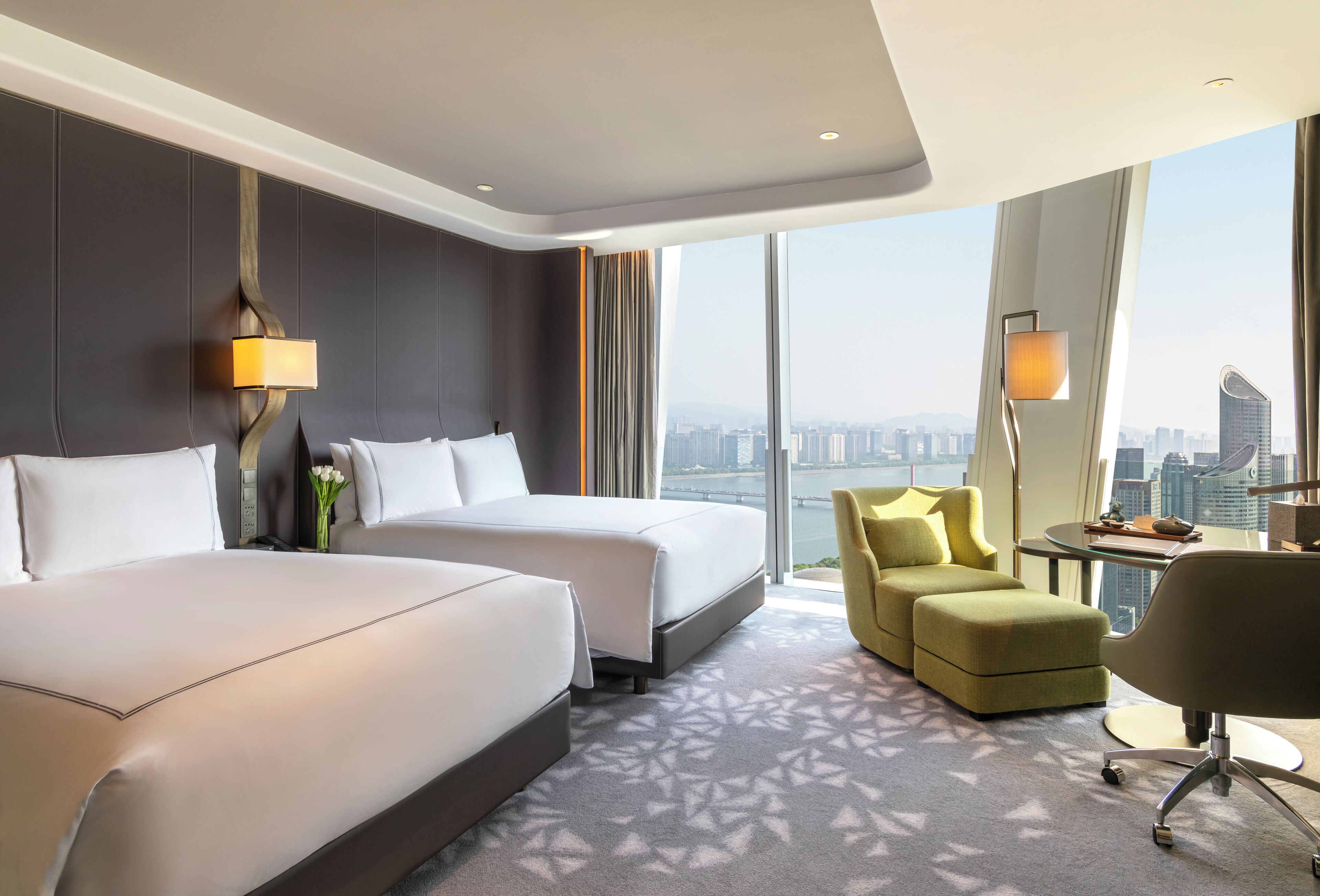 Une chambre d’hôtel avec deux lits, un canapé, un bureau et une vue sur le panorama urbain.