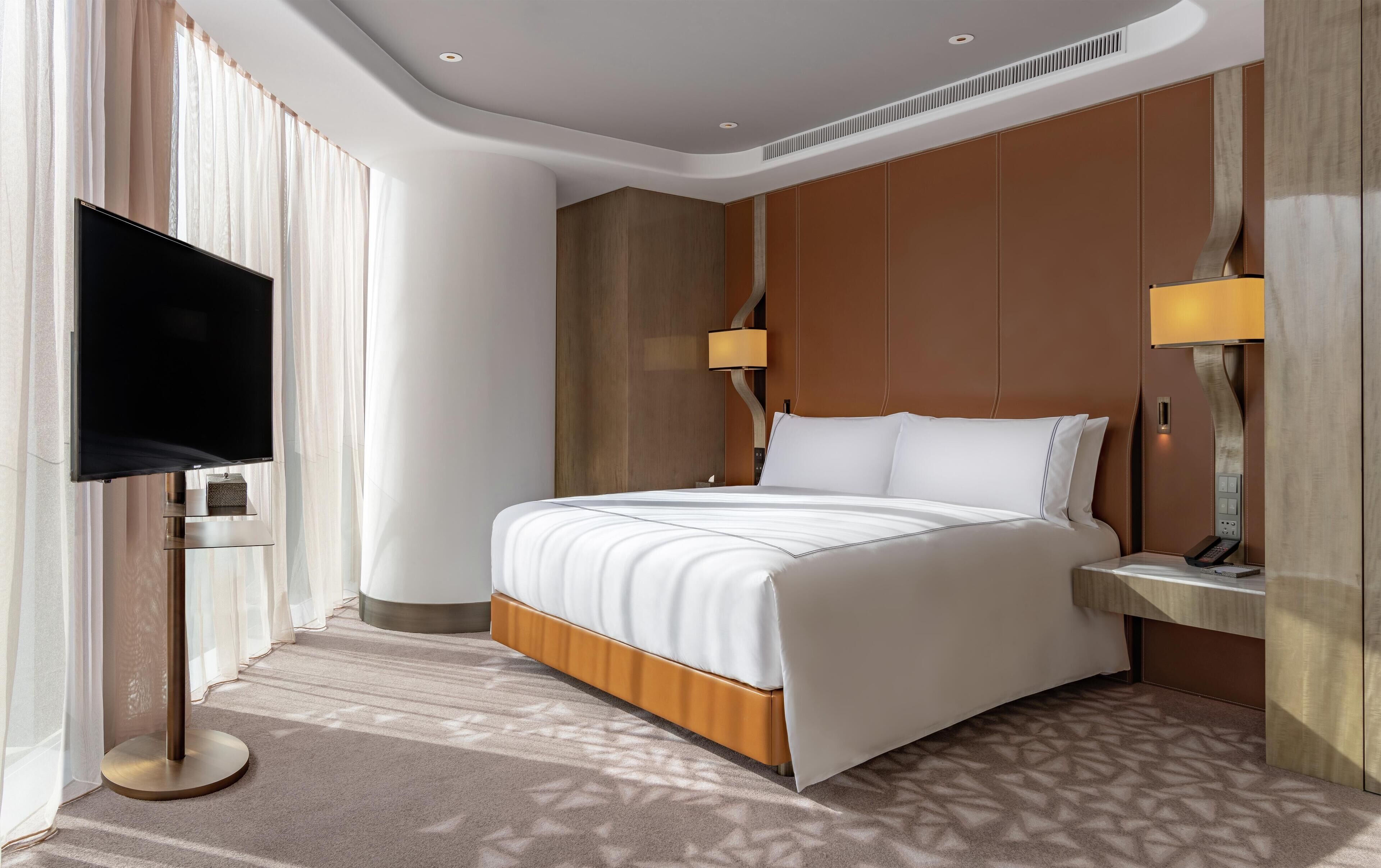 A modern hotel room with a large bed, a flat-screen TV, and two bedside lamps.