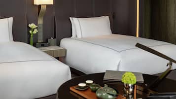 A hotel room with two beds, a bedside table with a lamp, a small vase with flowers, and a tray with teapots and cups.