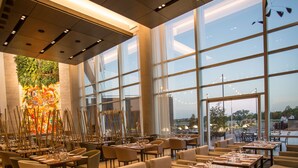 Ein modernes Restaurant mit hohen Decken, großen Fenstern und Blick auf die Stadtlandschaft.