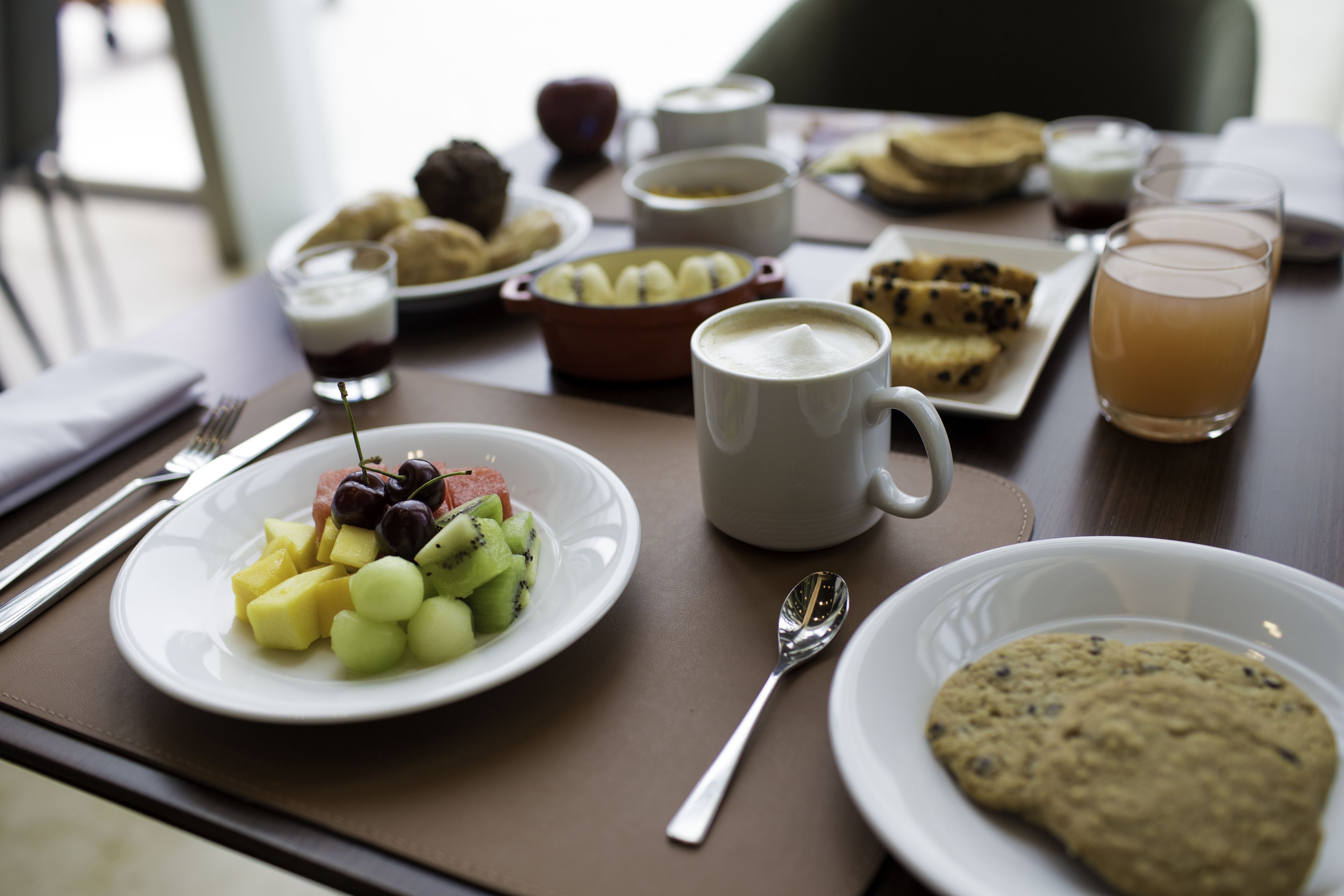 A breakfast table with various food items including fruits, cookies, and beverages.