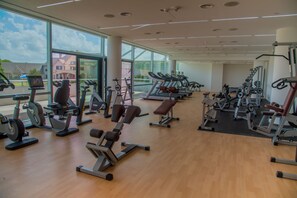 Ein großzügiges Fitnessstudio mit unterschiedlichen Trainingsgeräten, großen Fenstern und Holzboden.
