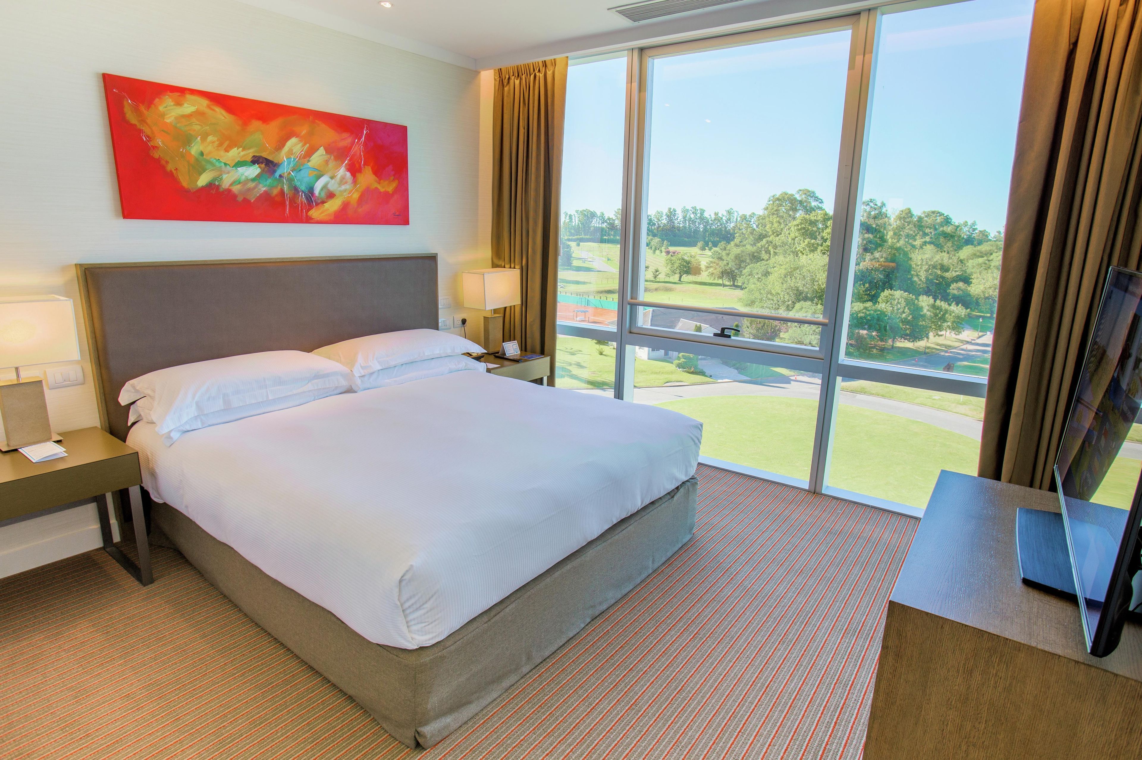 Habitación de hotel con una cama grande, un escritorio, un televisor y una ventana con vistas a un campo de golf.