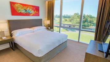 Habitación de hotel con una cama grande, un escritorio, un televisor y una ventana con vistas a un campo de golf.