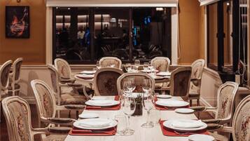 A dining area with tables set for service, chairs with floral upholstery, and a view of the dining area through a large window.