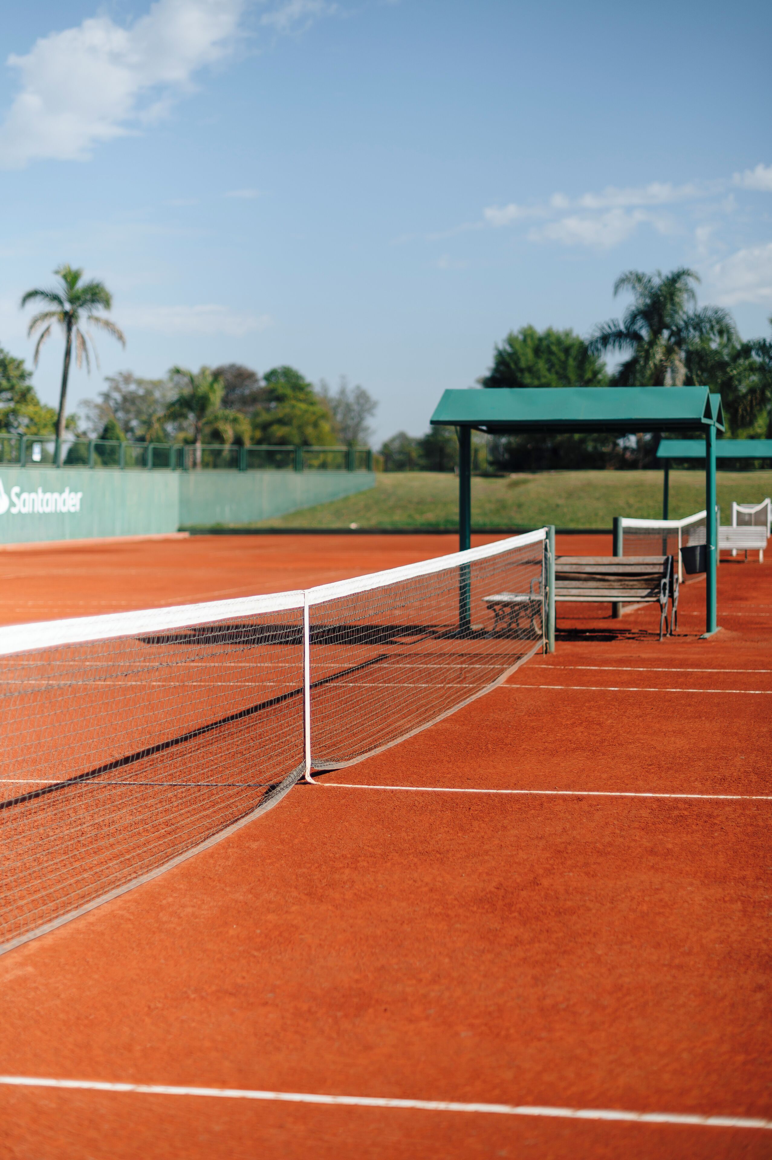 Tenniskenttä, jossa on verkko, penkkejä ja vihreä katos.